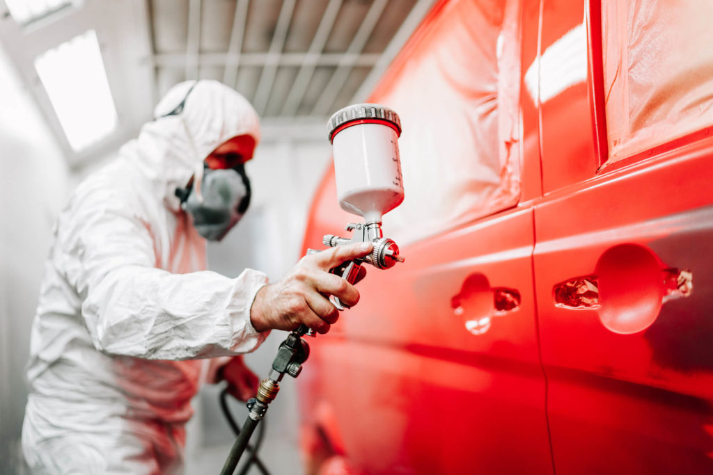 Close-up of worker using spray gun and airbrush and painting a red car